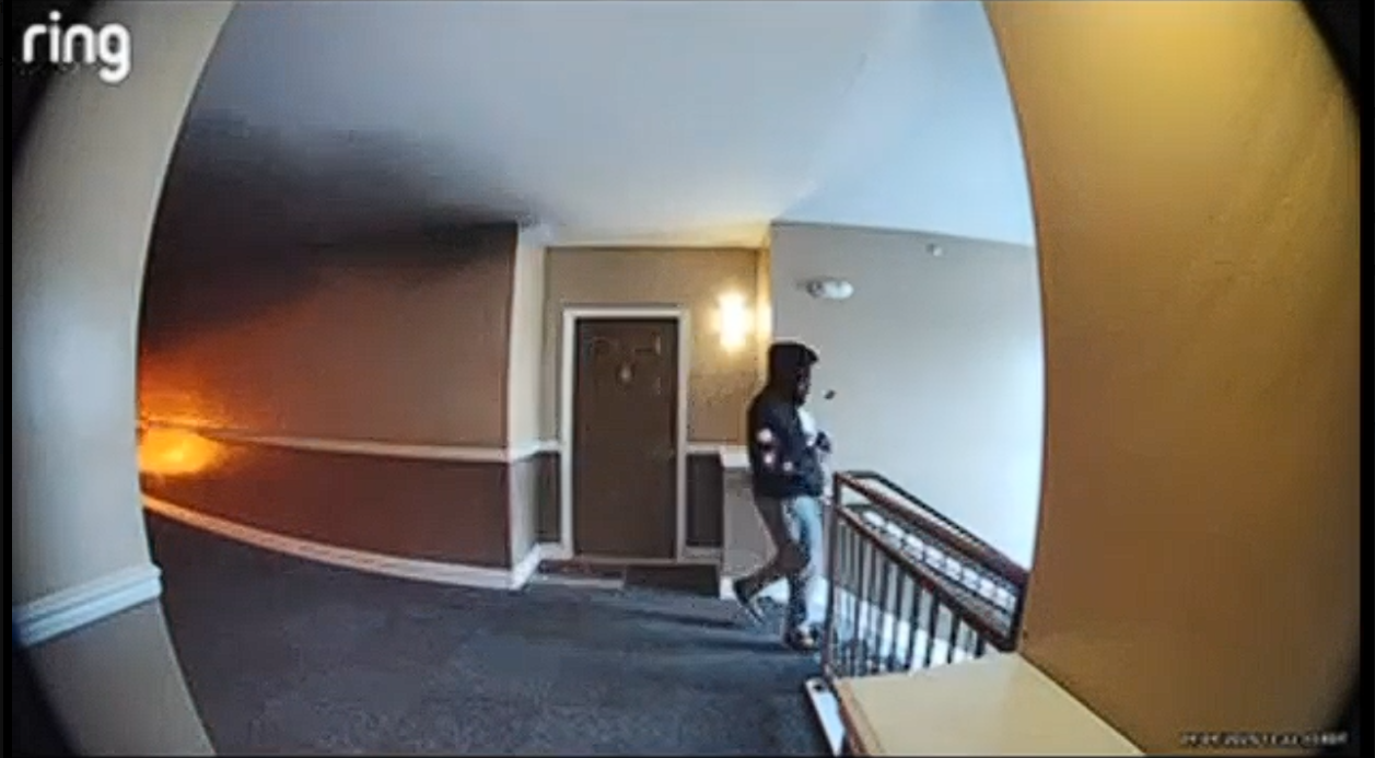 Defendant leaving the scene after setting fire with flames visible behind him in the hallway.